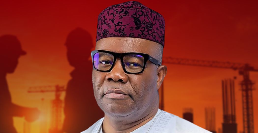 Nigerian man in white traditional attire and a patterned red cap, against an orange construction-site background with silhouettes in the distance.