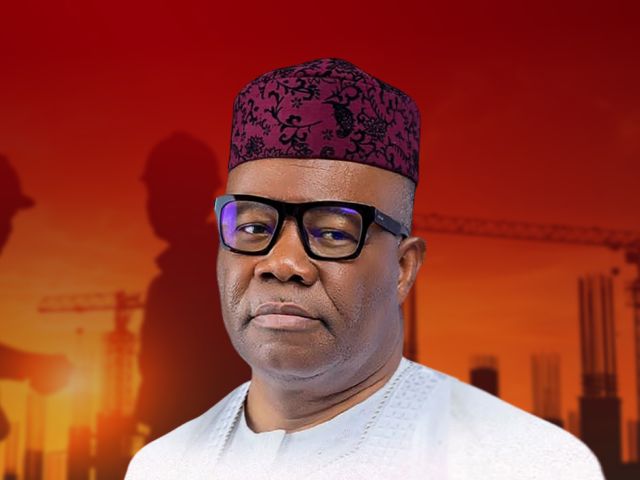 Nigerian man in white traditional attire and a patterned red cap, against an orange construction-site background with silhouettes in the distance.